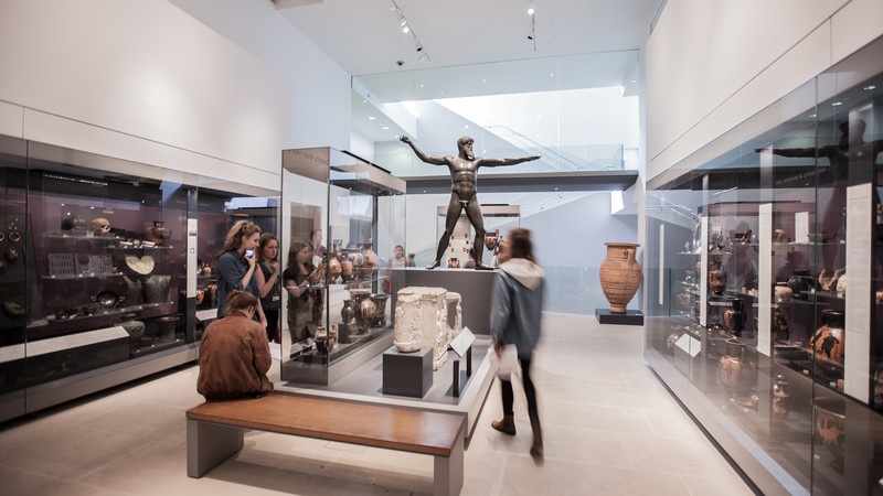 A gallery inside the Ashmolean Museum in Oxford showing people viewing a sculpture and objects in display cases.